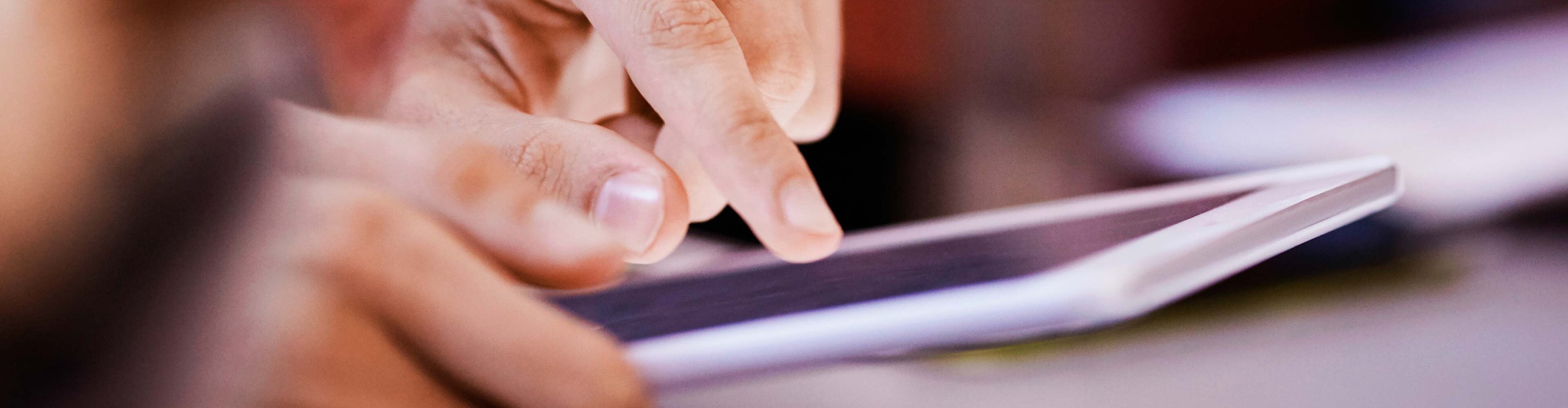 Eine Hand tippt auf einem Tablet. Die Finger sind deutlich zu sehen, während der Bildschirm im Hintergrund leicht erleuchtet ist. Das Bild vermittelt den Eindruck von Aktivität und Interaktion mit digitaler Technologie.