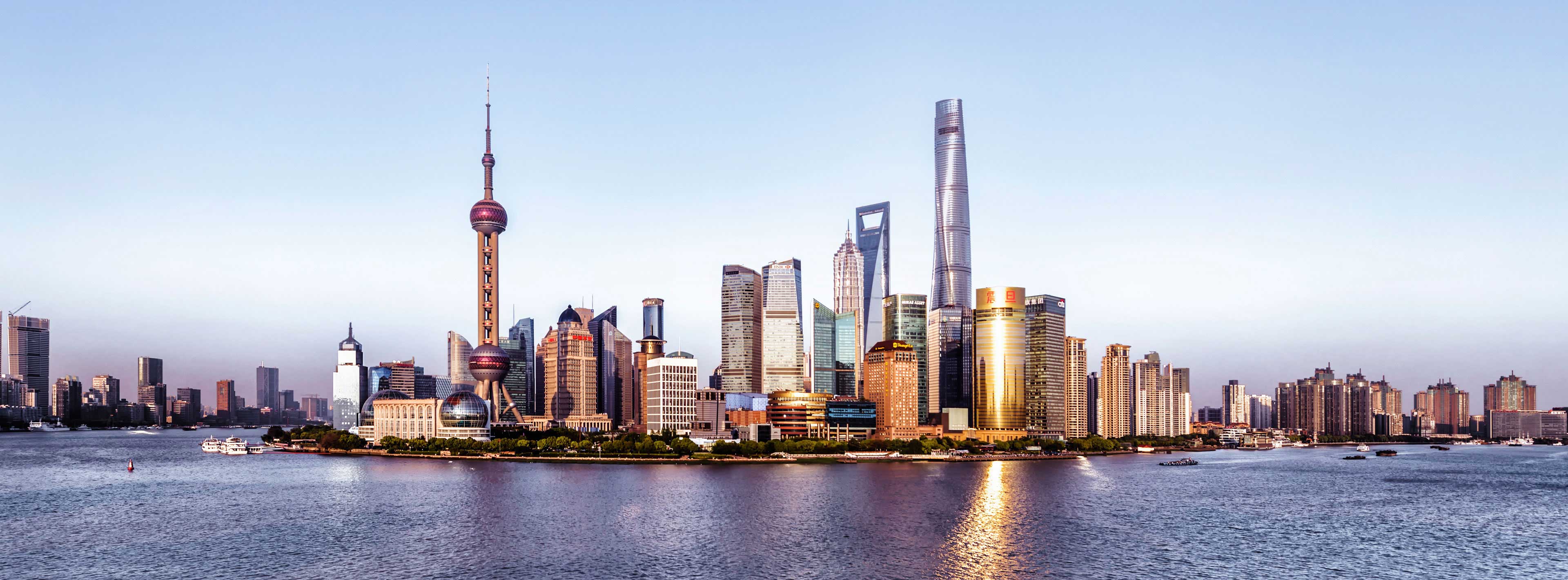 A panoramic view of Shanghai's skyline at dusk, showcasing a mix of modern skyscrapers, including notable towers. The skyline is reflected in the water, enhancing the city's vibrant atmosphere. The scene captures the dynamic essence of urban life along the Huangpu River.
