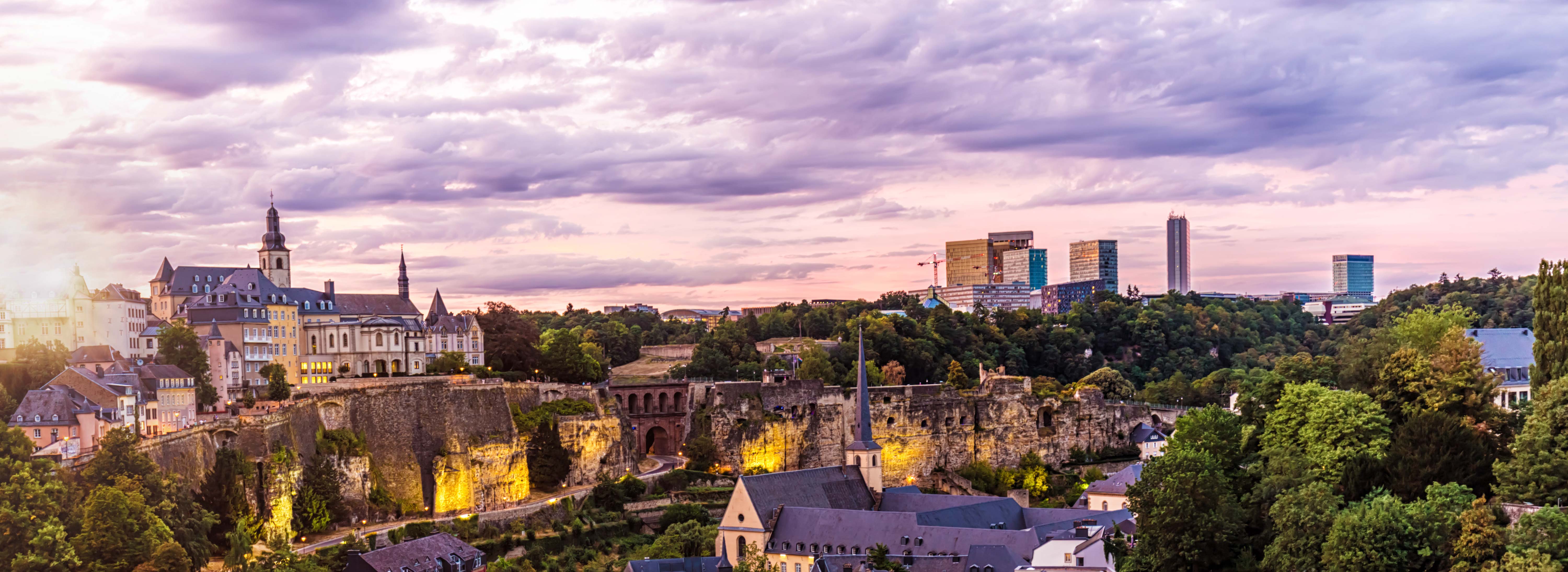 Eine malerische Panoramaansicht einer Stadt mit historischen Gebäuden, einschließlich einer Kirche mit einem hohen Turm, und modernen Wolkenkratzern im Hintergrund. Die Architektur skizziert eine harmonische Verbindung von Alt und Neu, während der Himmel in sanften Farben erleuchtet ist.