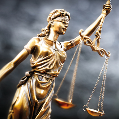 A bronze statue of Lady Justice, blindfolded, holding a pair of scales. She symbolizes impartiality and fairness in the justice system, representing the idea that justice should be administered without bias. The background is blurred, focusing on her figure and scales.